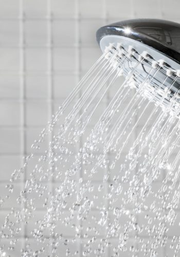 Shower head with running water in white bathroom. Copy space